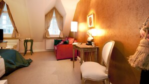 Habitació d'hotel amb llit, escriptori, cadira, sofà, làmpada i finestra amb cortines.