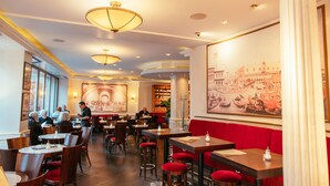 Un restaurant amb diverses taules i seients aïllats, seients tapissats de color vermell i un mural gran a la paret.