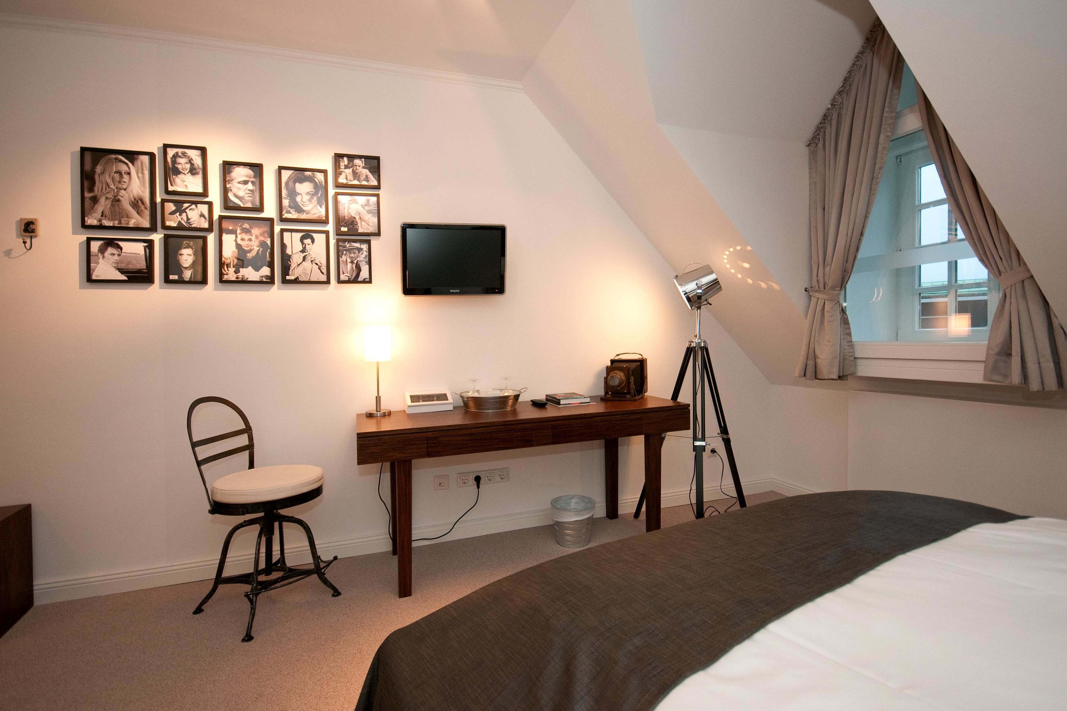 Une chambre à coucher avec un lit, un bureau avec une chaise, une télévision et des tableaux encadrés accrochés au mur.