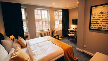 Ein Hotelzimmer mit einem großen Bett, zwei Nachttischen, einem Schreibtisch mit Stuhl und einem Vorhangfenster.