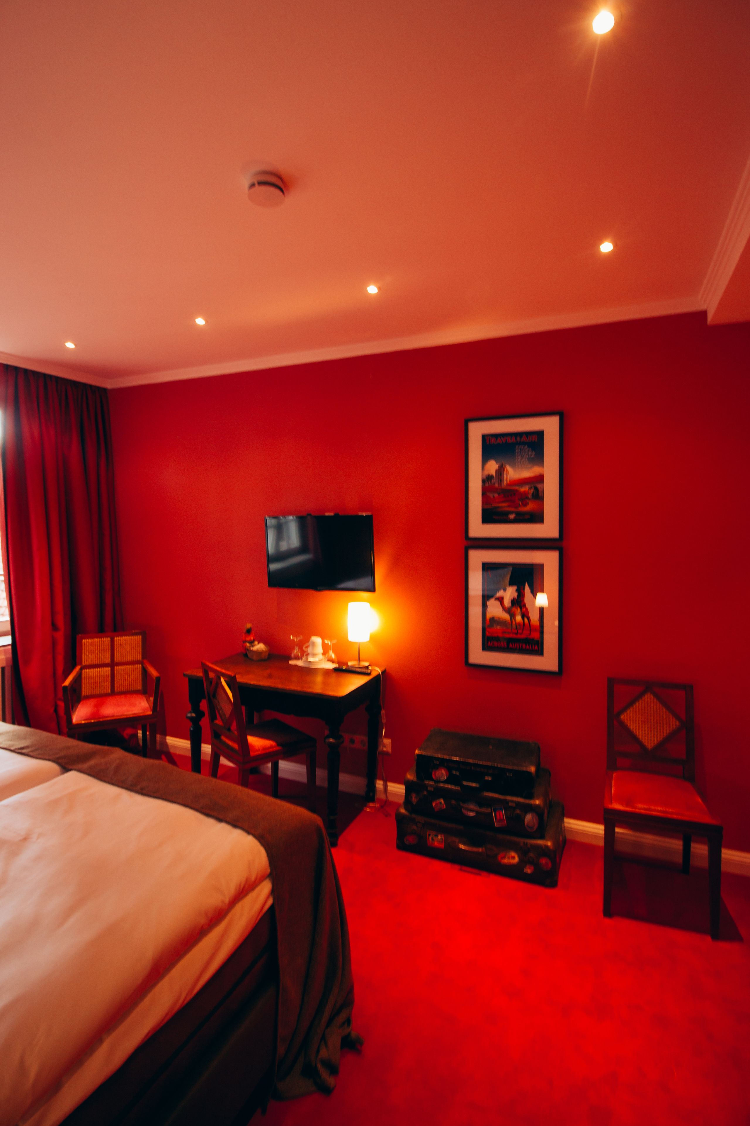 Habitación de hotel con cama, escritorio con lámpara, televisión y dos cuadros en la pared.