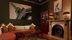 A living room with a red sofa, a fireplace, a large painting of the Eiffel Tower, and a cabinet with glass doors.