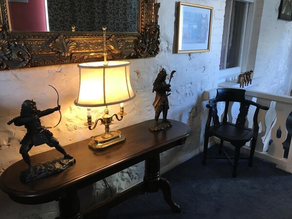 A wooden table with a lamp and two figurines, a chair, and a mirror with ornate detailing.