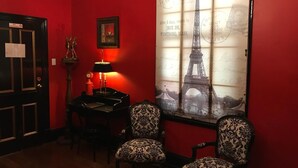 A room with a red wall, a framed picture of the Eiffel Tower, two patterned chairs, a desk with a lamp, and a door with a 'No Smoking' sign.
