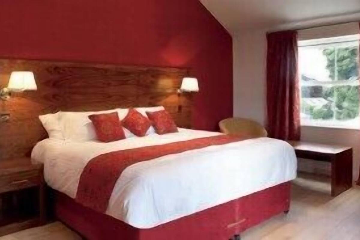 A hotel room with a large bed, two bedside lamps, a window with curtains, and a chair.