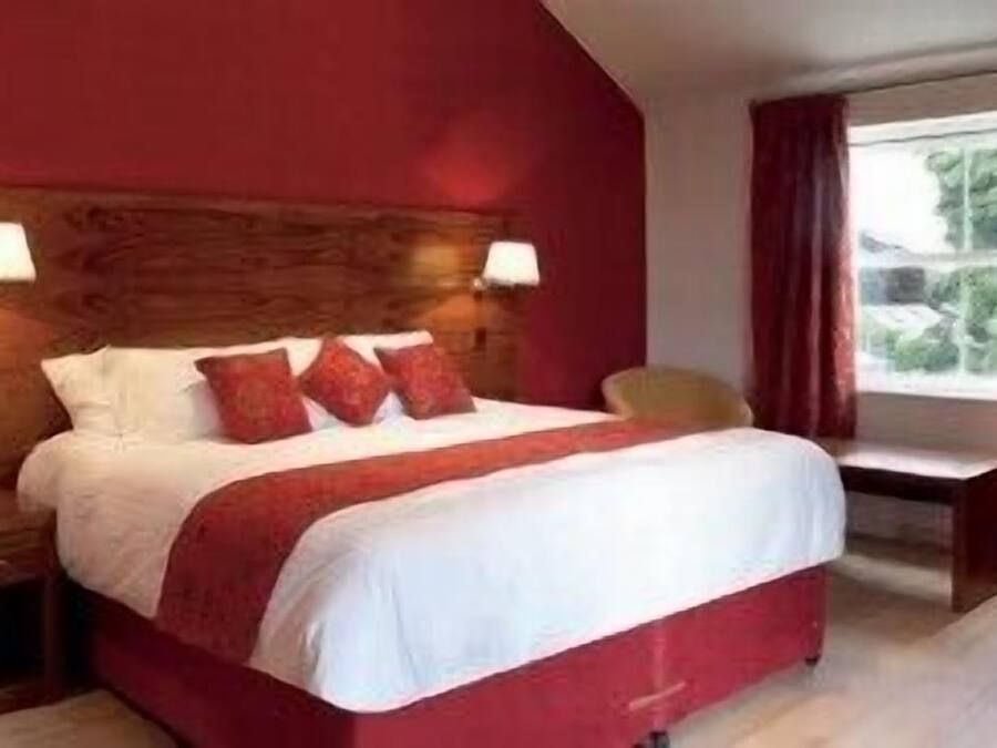 Ein Hotelzimmer mit einem großen Bett, zwei Nachttischlampen, einem Fenster mit Vorhängen und einem Sessel.