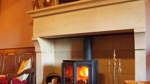 A cozy room with a wood-burning stove, a chair with a red cushion, and a table with a candle. - Black Swan Inn (Ripon)