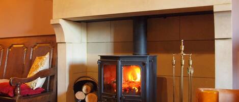 A cozy room with a wood-burning stove, a chair with a red cushion, and a table with a candle.