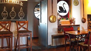 A cozy pub interior with wooden furniture, a bar area with taps labeled 'Theakston Best', 'Shepherd Sitting', and 'Black Sheep', and a clock on the wall. - Black Swan Inn (Ripon)