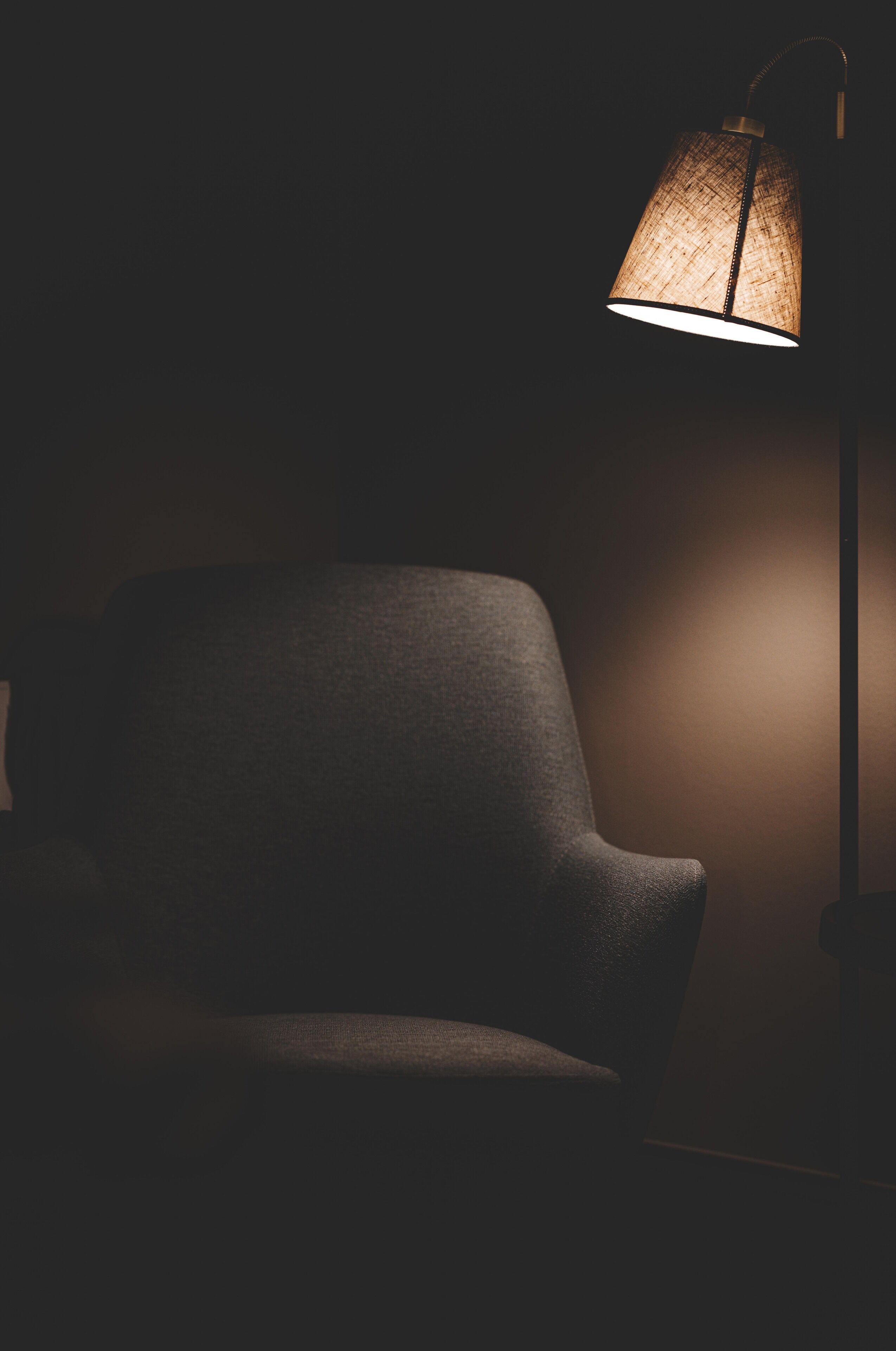 Une pièce sombre, avec une seule chaise et une lampe suspendue qui diffuse une lumière chaleureuse.