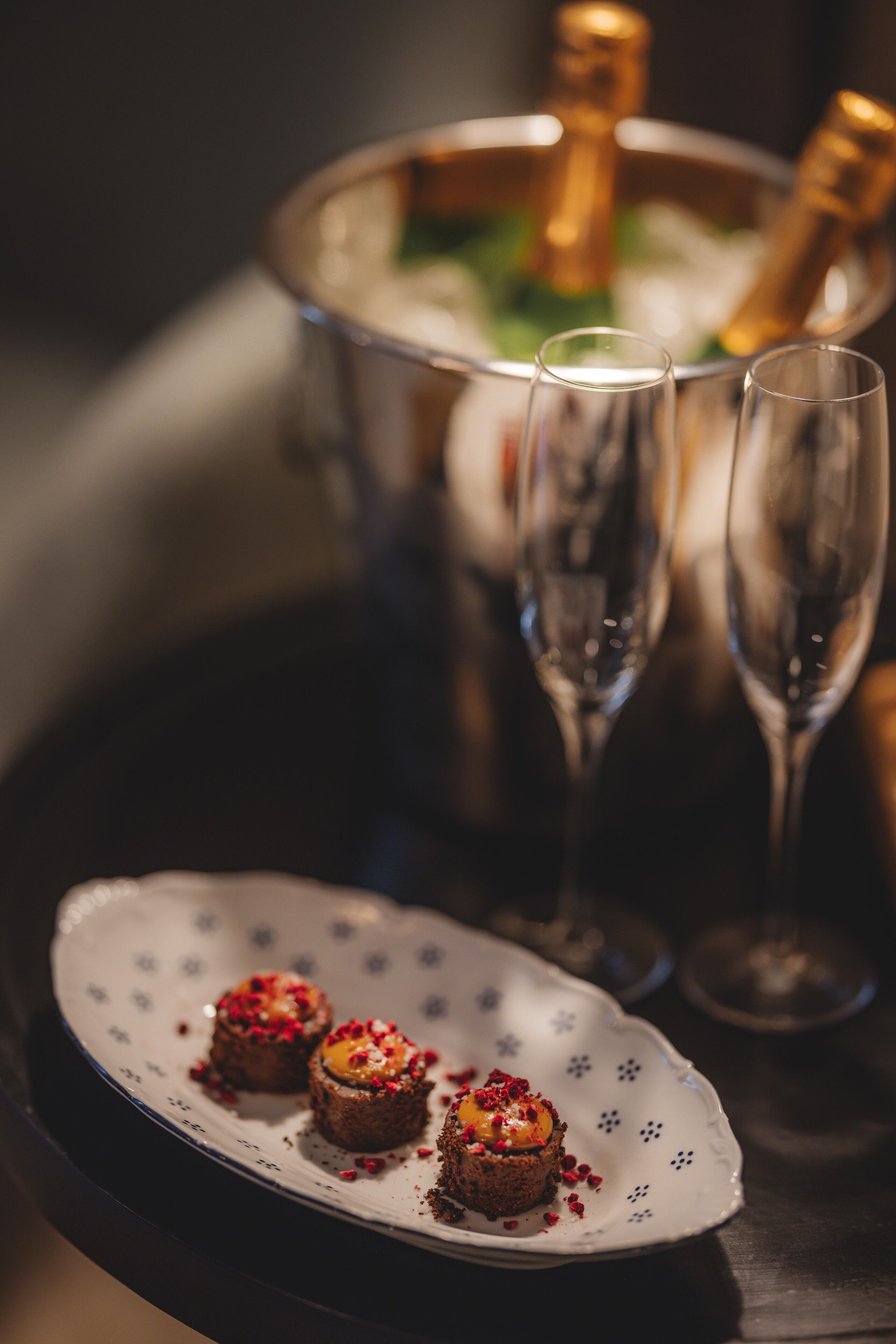 A dessert plate with three small cakes, a champagne bucket, and two champagne flutes.