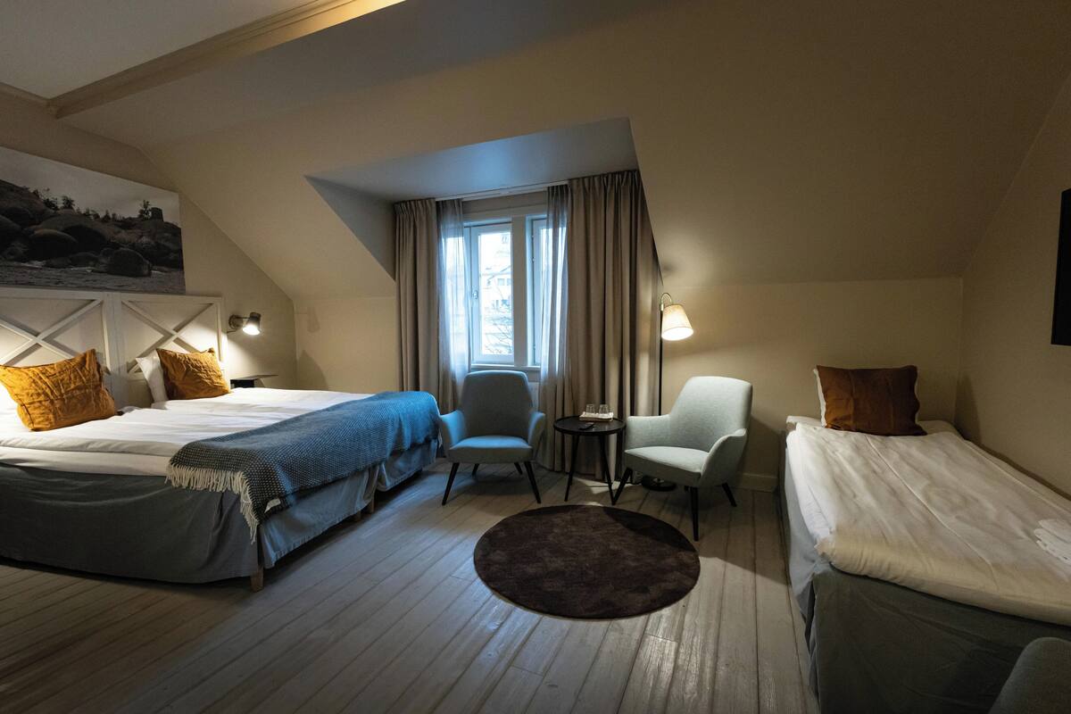 Una habitación de hotel con dos camas, un pequeño tapete redondo, una silla y una mesa.