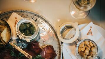 A dining table with a metal tray holding a jar of olives, a jar of almonds, and some bread.