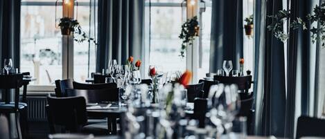 Un restaurante con mesas dispuestas para comer, ventanas amplias y plantas colgantes.