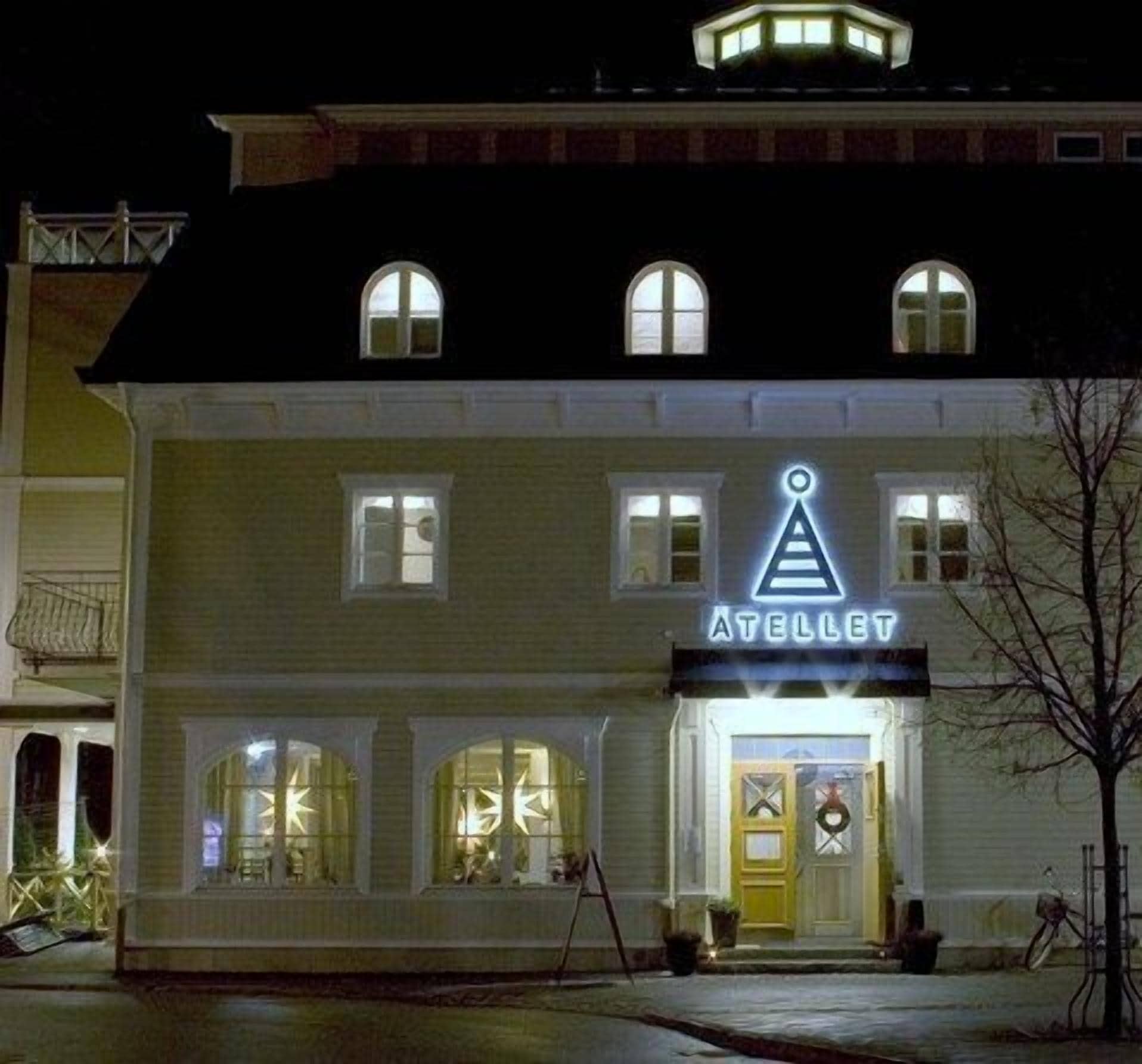 En byggnad med en neonskylt som visar ordet ”ATELLIET” och en triangulär logotyp ovanför ingången.