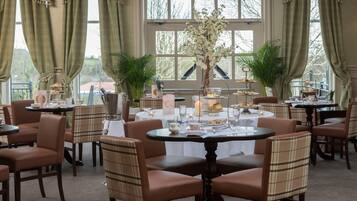 A dining area with round tables, brown upholstered chairs, and floral centerpieces.