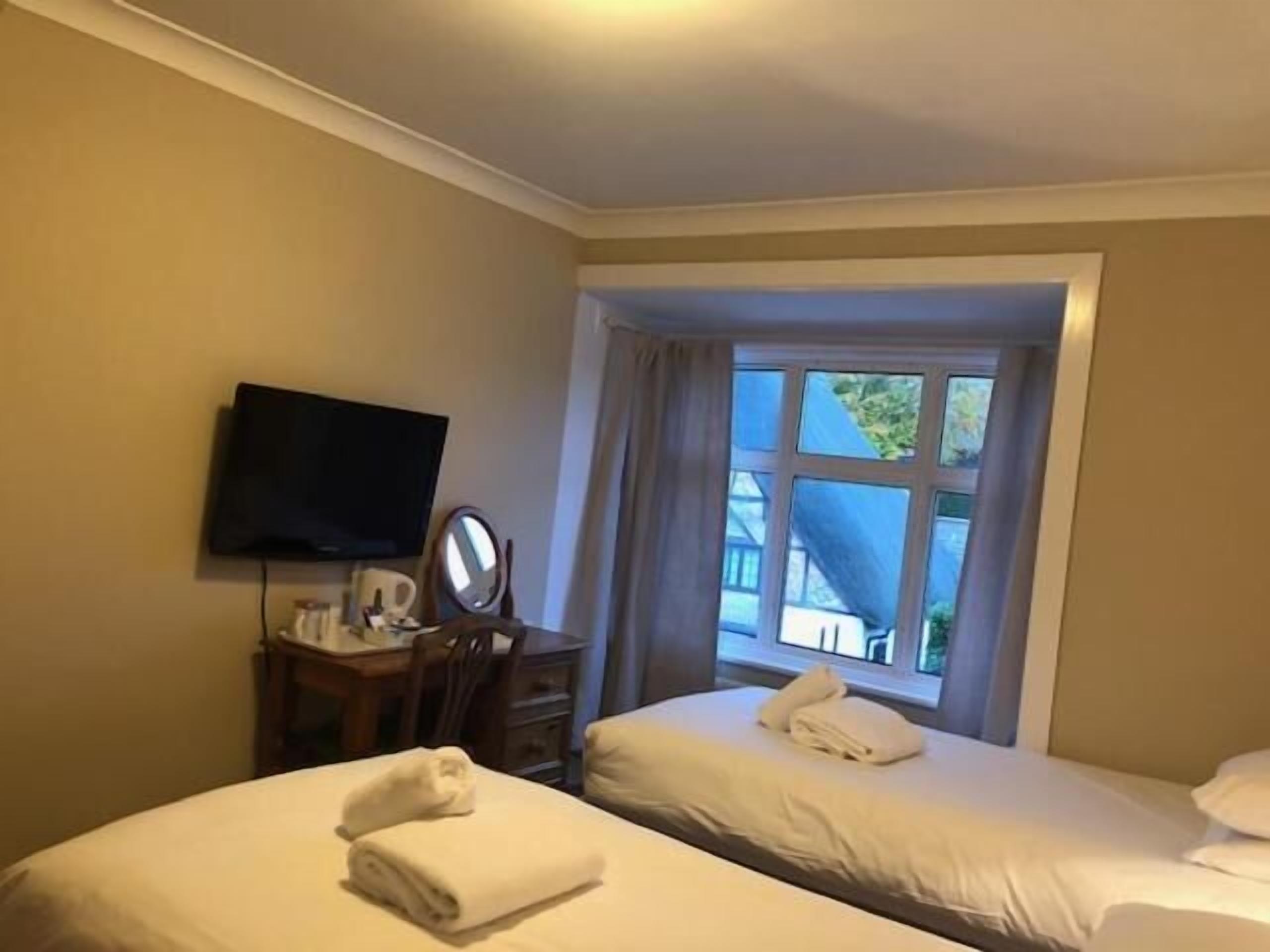 A hotel room with two beds, a television, a mirror, and a window with curtains.