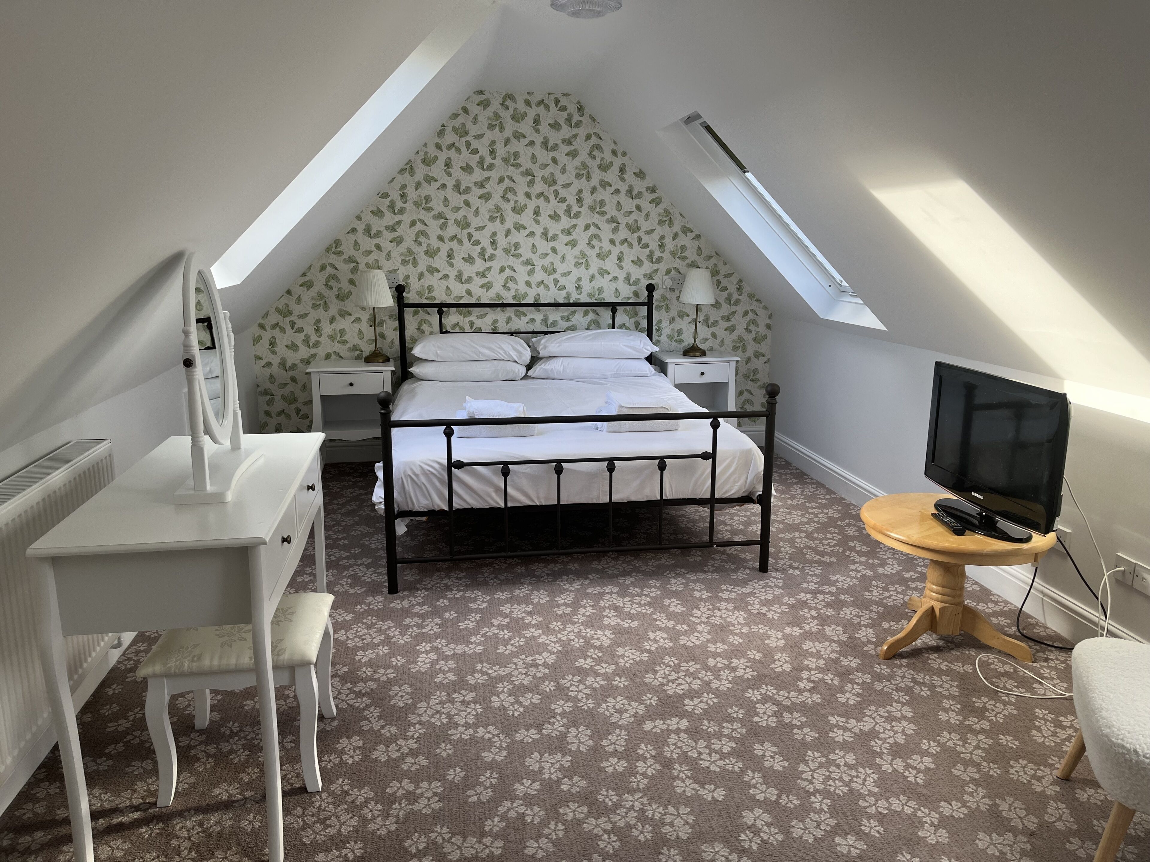 A bedroom with a sloped ceiling, a bed, a desk, a chair, a TV, and a small table.