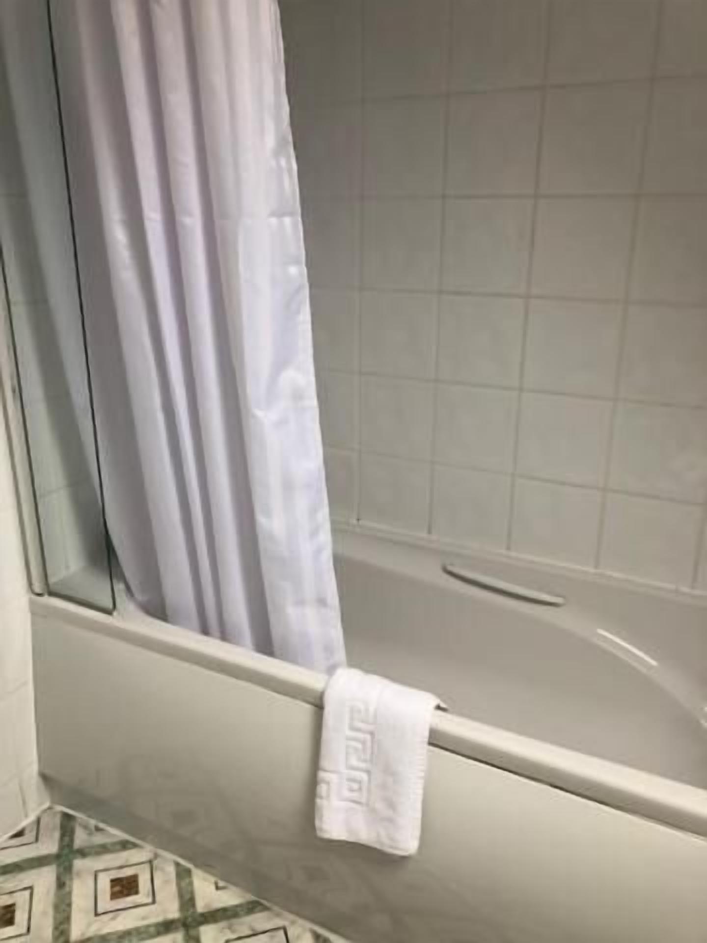 Un baño con una bañera, una toalla blanca colgada a un lado y un suelo con diseño.