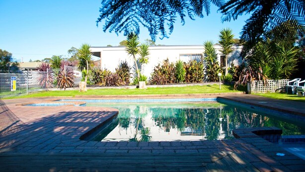 Una piscina con un riflesso limpido, circondata da un giardino curato e con diverse piante, oltre a un recinto.