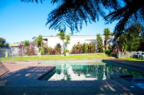 A swimming pool with a clear reflection, surrounded by a well-maintained garden with various plants and a fence. - Motel Marengo (Marengo)