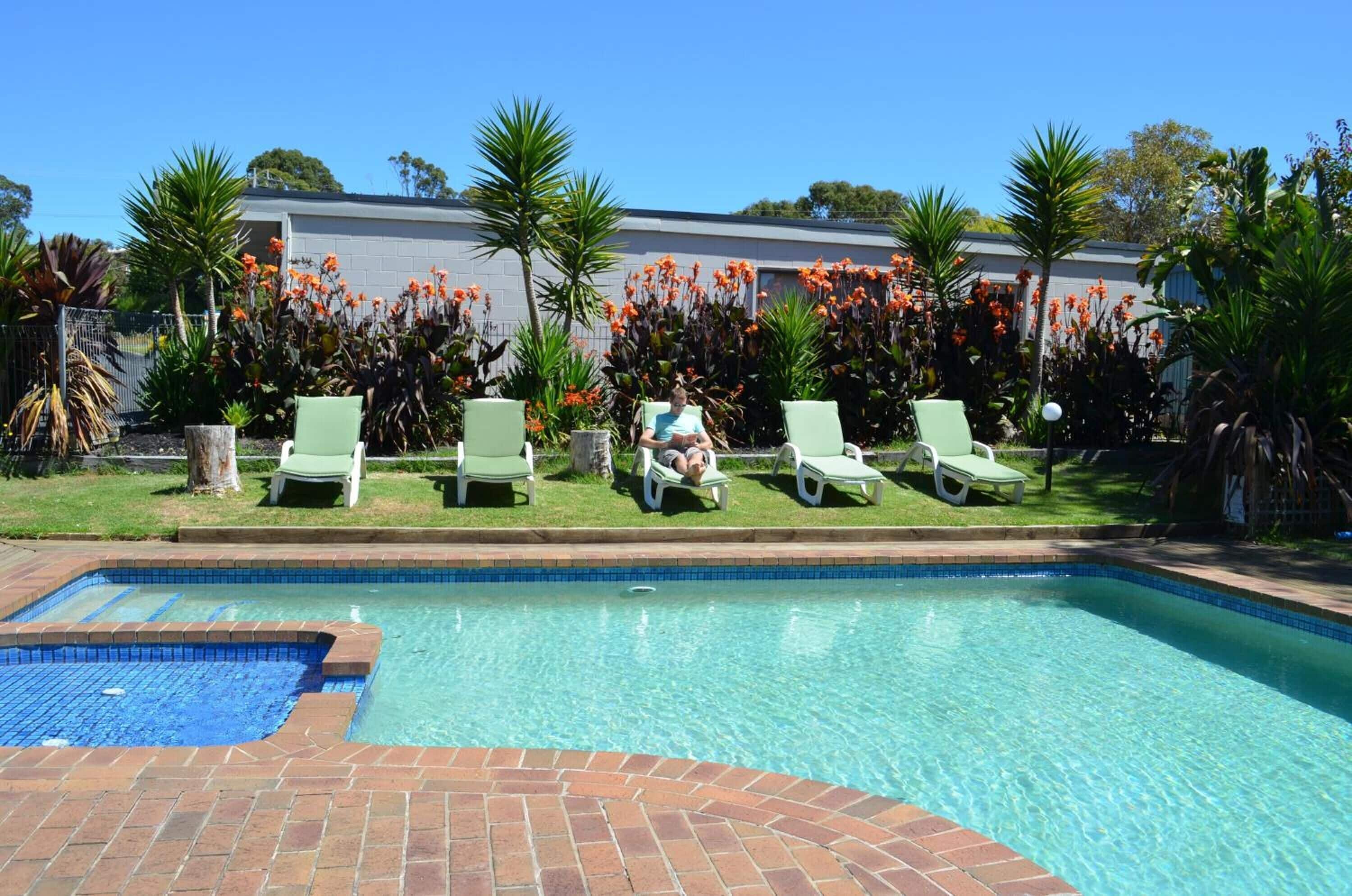 A swimming pool with a tiled edge, surrounded by green lounge chairs and tropical plants.