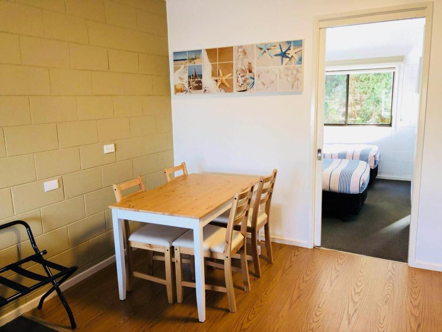 A room with a wooden dining table, four chairs, a black folding chair, and a wall with a nautical-themed artwork.