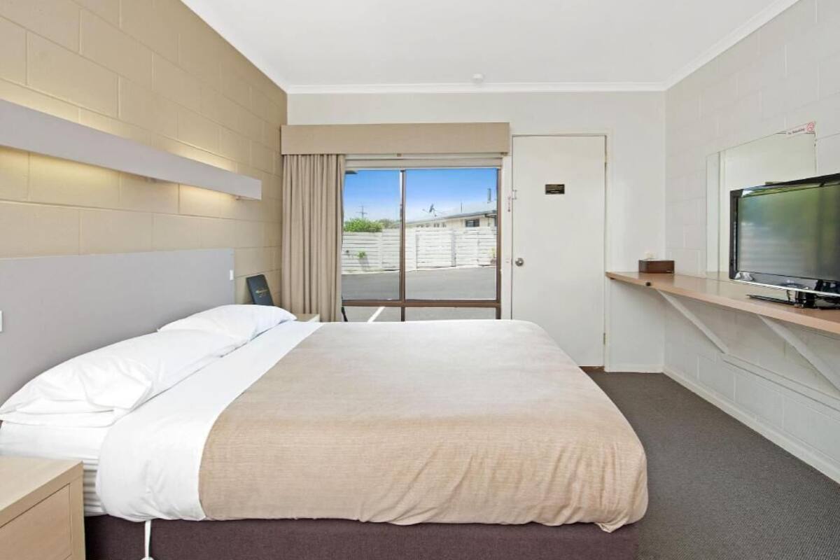 A hotel room with a bed, a television, a window with curtains, and a door.