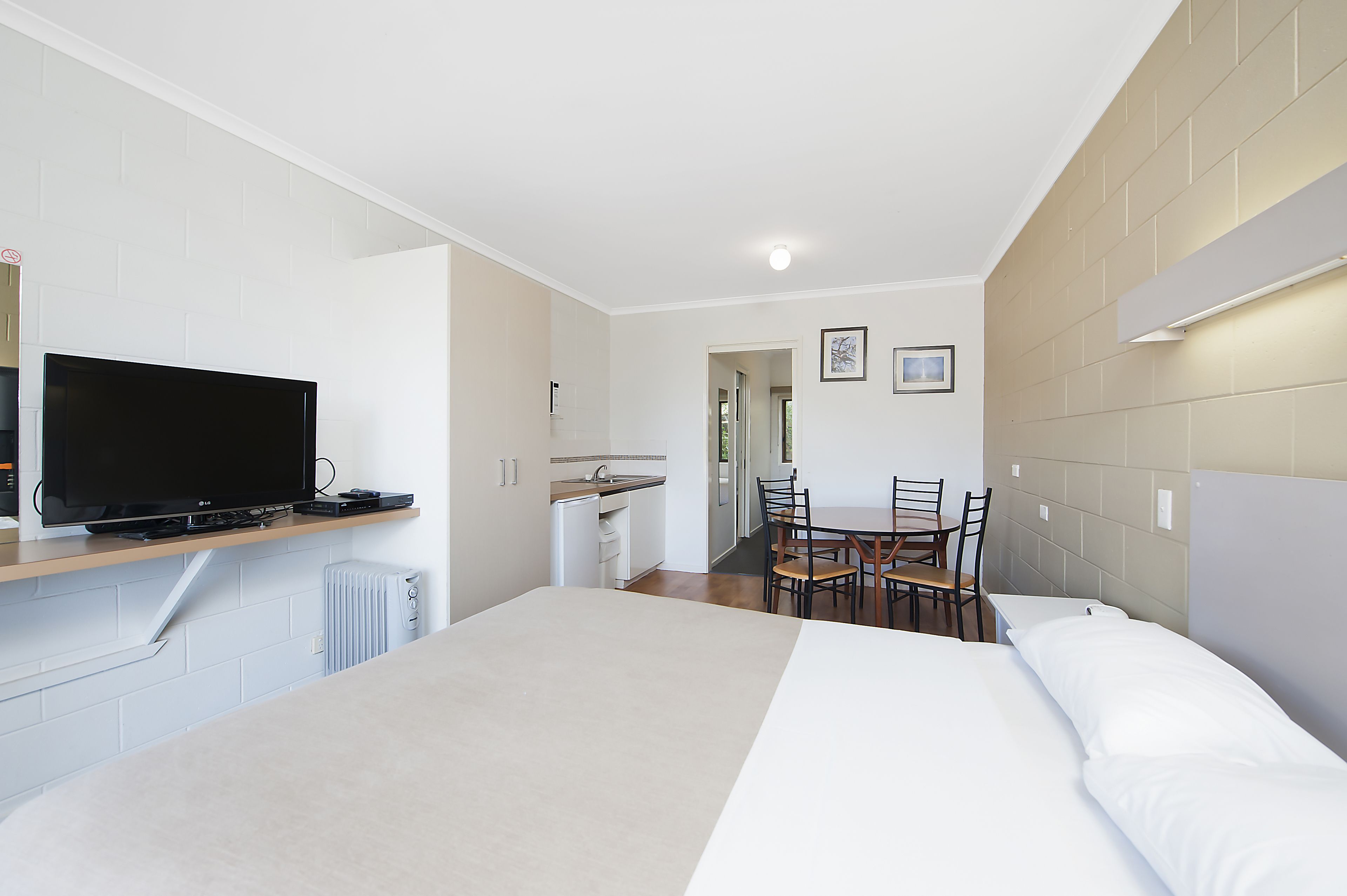 Una habitación de hotel con cama, televisor, mesa de comedor con sillas y kitchenette.