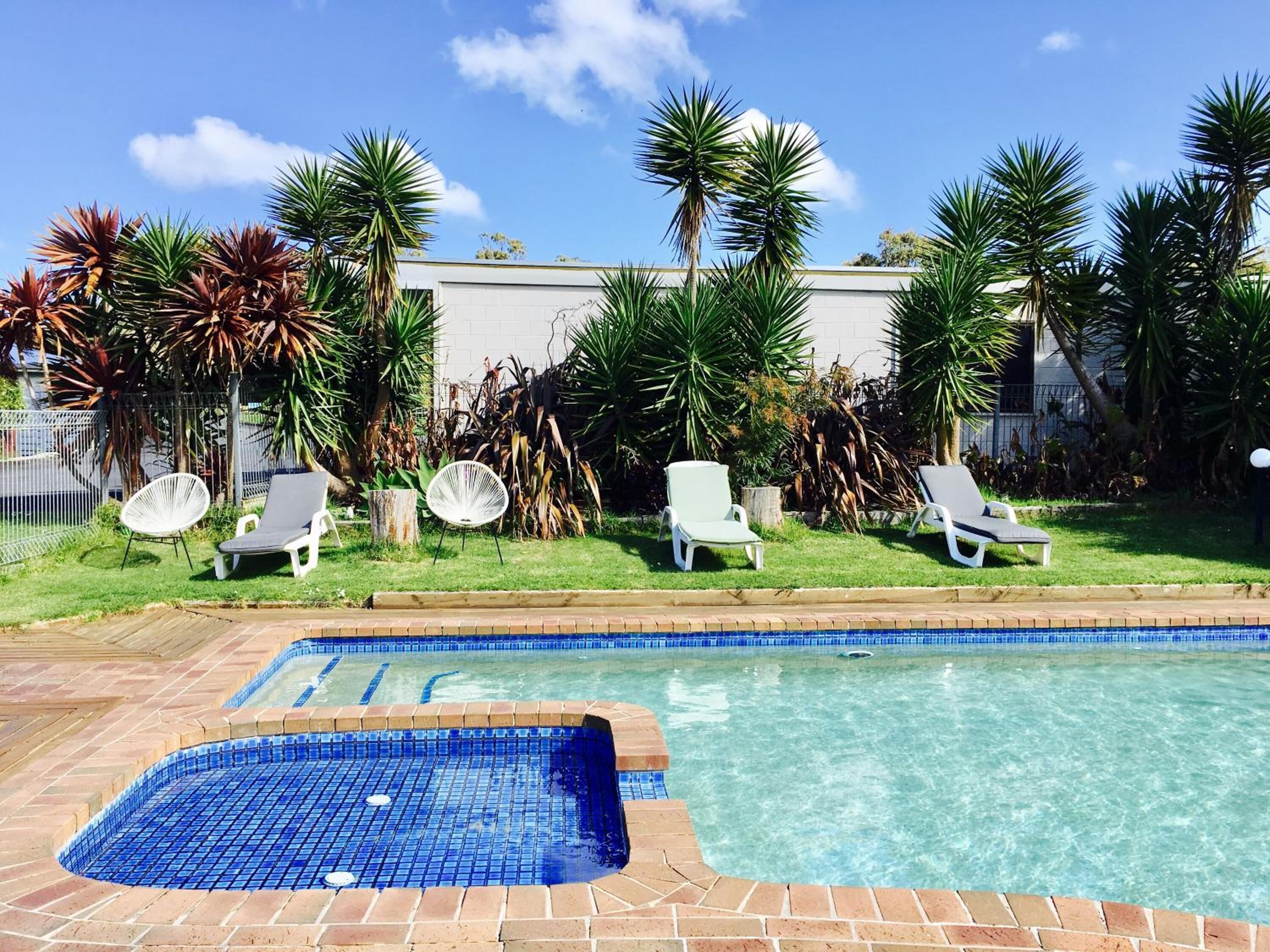 A swimming pool with a tiled deck, surrounded by palm trees and lounge chairs.