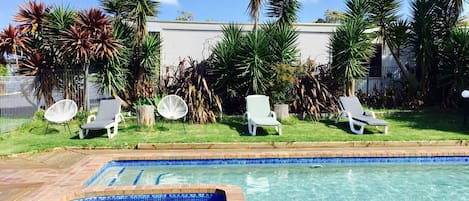 Una piscina con bordo piastrellato, circondata da palme e poltrone da relax.