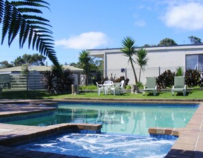 A swimming pool with a hot tub, surrounded by a patio area with chairs and a table. - Motel Marengo (Marengo)