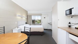 Una camera d'albergo compatta con un letto, un tavolino, una sedia, un forno a microonde e un frigorifero.