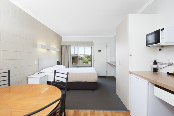 A compact hotel room with a bed, a small table, a chair, a microwave, and a refrigerator. - Motel Marengo (Marengo)