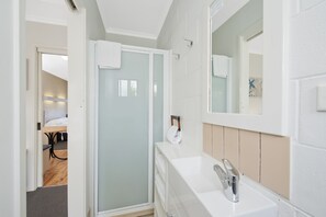 A modern bathroom with a glass shower enclosure, a white sink, and a large mirror. - Motel Marengo (Marengo)