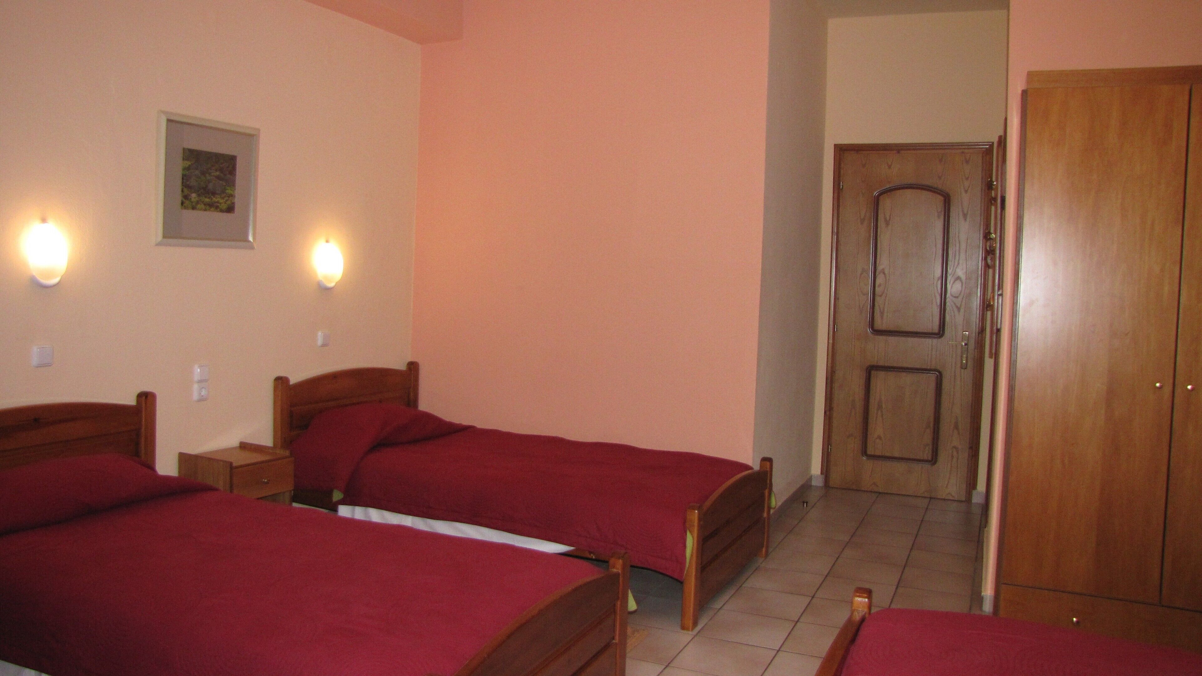 Una habitación con dos camas de madera, cada una con una colcha roja, un armario de madera y una puerta.