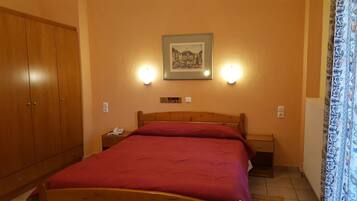 Habitación de hotel con una cama de madera, una mesita de noche, un teléfono y un cuadro enmarcado en la pared.