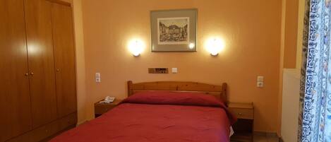 Habitación de hotel con una cama de madera, una mesita de noche, un teléfono y un cuadro enmarcado en la pared.