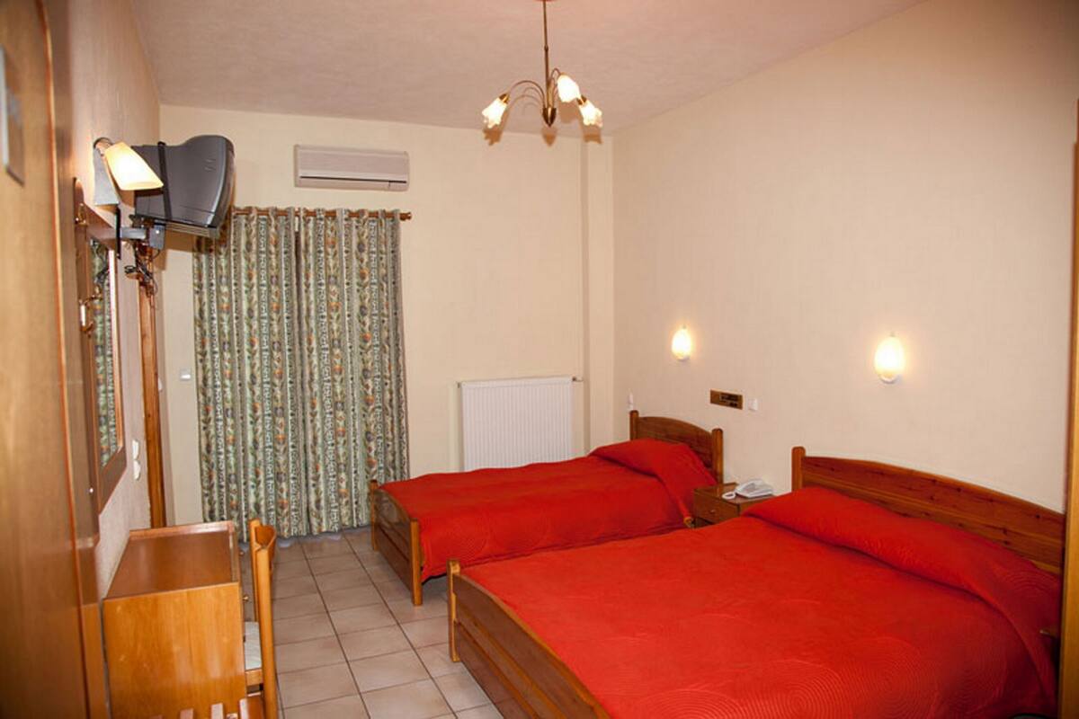 Una habitación con dos camas individuales, un escritorio de madera, una silla, una lámpara, un radiador y una cortina.