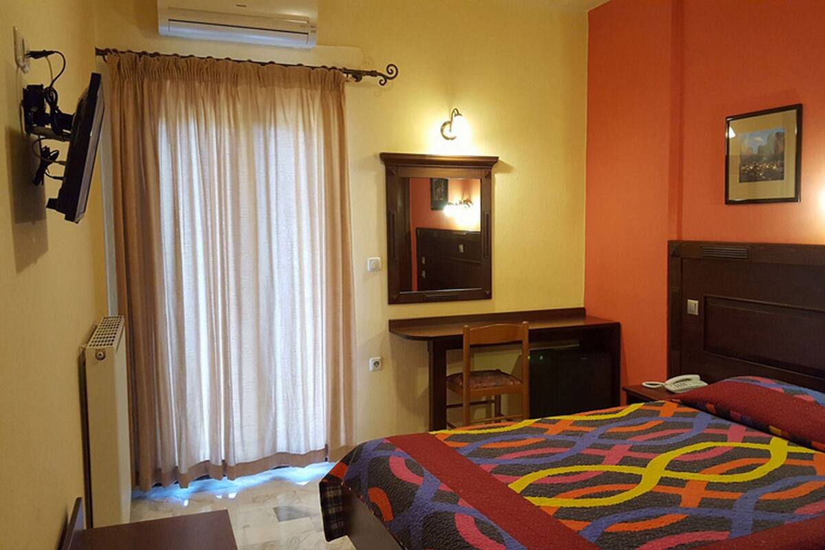 Habitación de hotel con cama, escritorio, silla, espejo, teléfono y un cuadro en la pared.