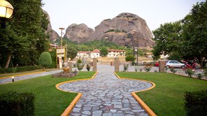 A paved pathway leading to a building with a star-shaped design, surrounded by greenery and a mountainous backdrop. - Spanias (Kalabaka)