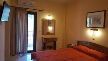 Habitación de hotel con cama, escritorio, silla, televisor, espejo y un cuadro en la pared.