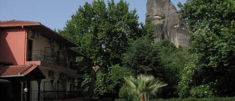 Un edificio con fachada roja, balcones y un jardín con una palmera y rocas.