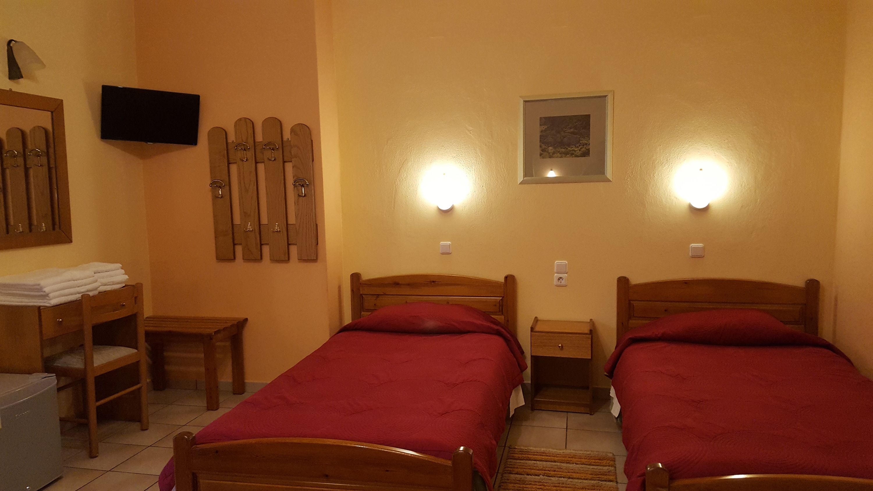 Une chambre avec deux lits en bois, une petite table, une chaise, un téléviseur et un porte-skis.