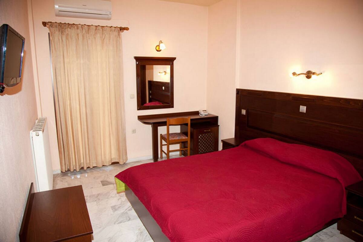 Un dormitorio con cama, escritorio, silla, espejo y mesita de noche.