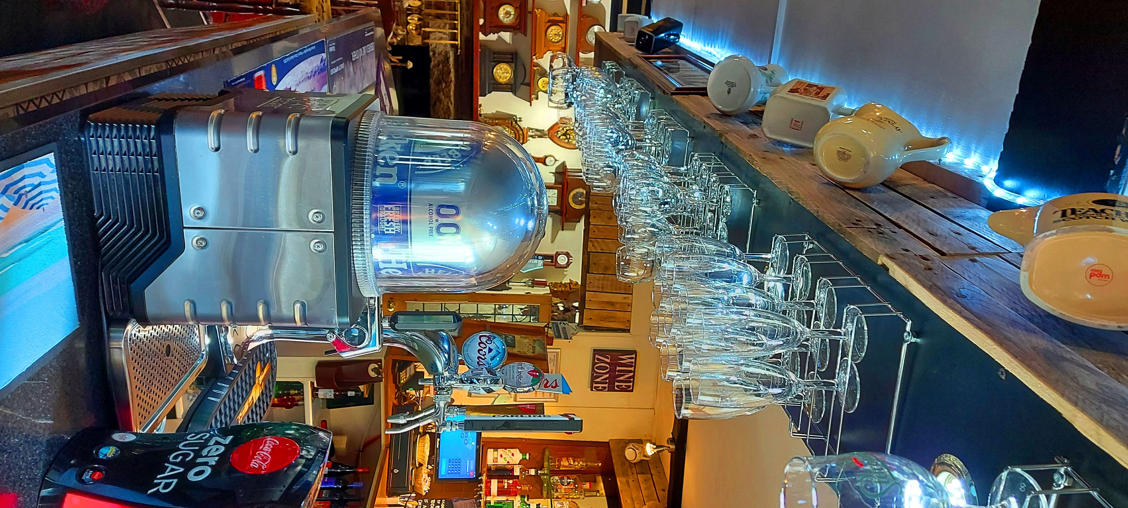 A bar area with a large beer tap, multiple wine glasses, and a variety of bottles and bottles.