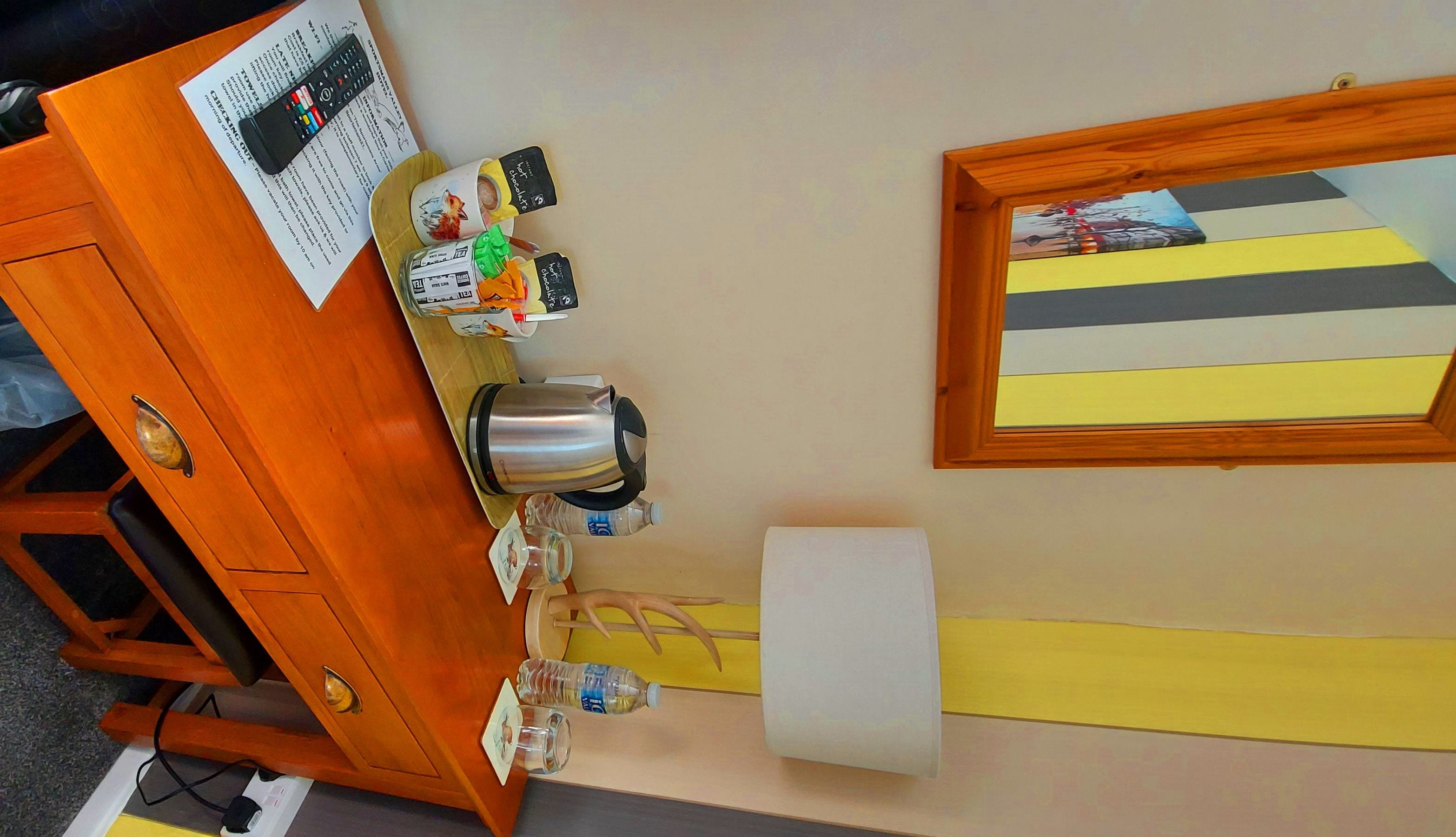 A wooden cabinet with a coffee maker, tea bags, and a framed picture on the wall.