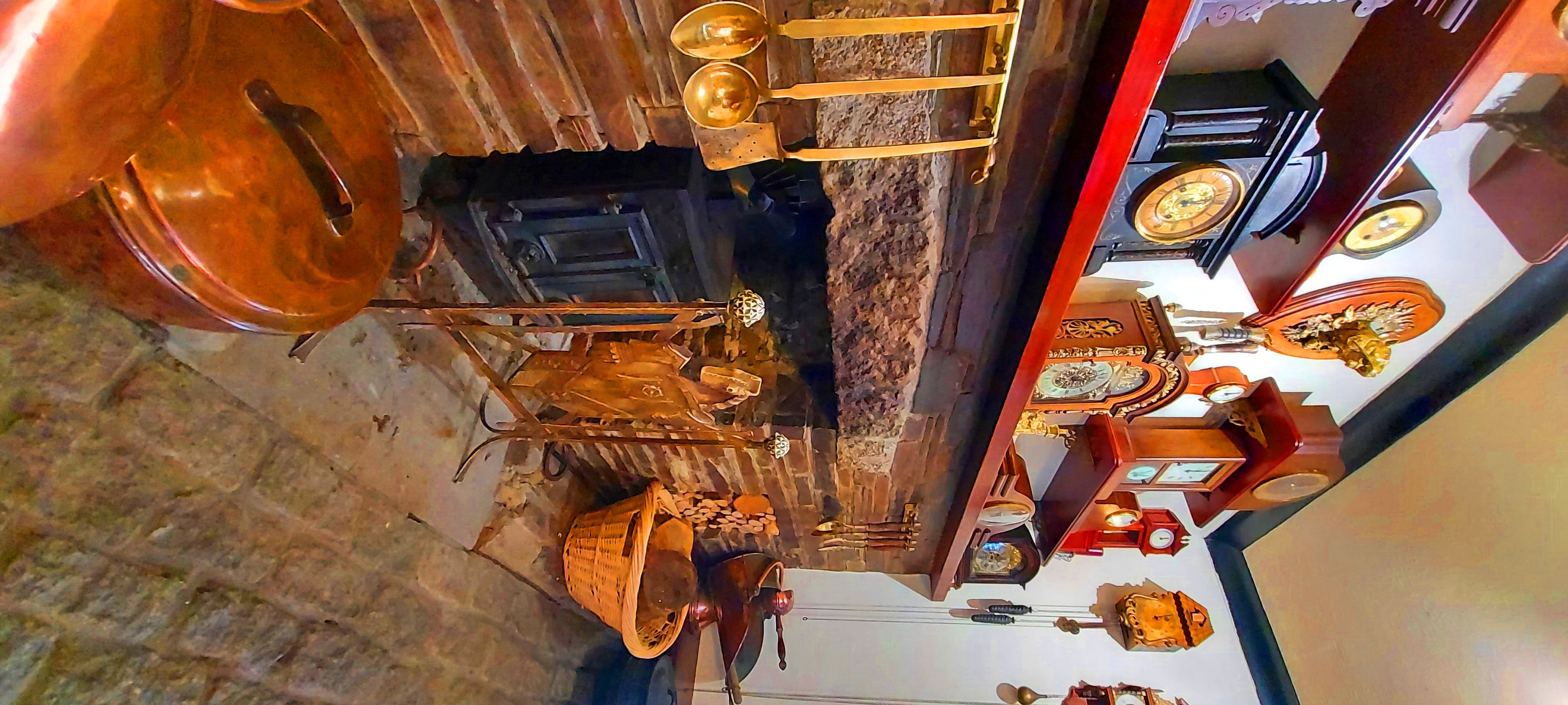 Ein Zimmer mit rustikalem Interieur, das eine Steinwand, eine Holztür und eine Metalllüster zeigt. Auf einem kleinen Tisch stehen ein Korb und eine Flasche.
