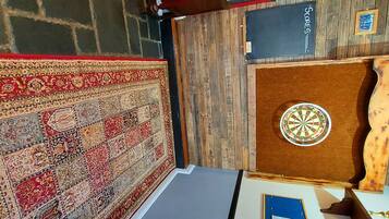 Una habitación con alfombra estampada, un dardo y una pizarra con la palabra 'SCORES' escrita.