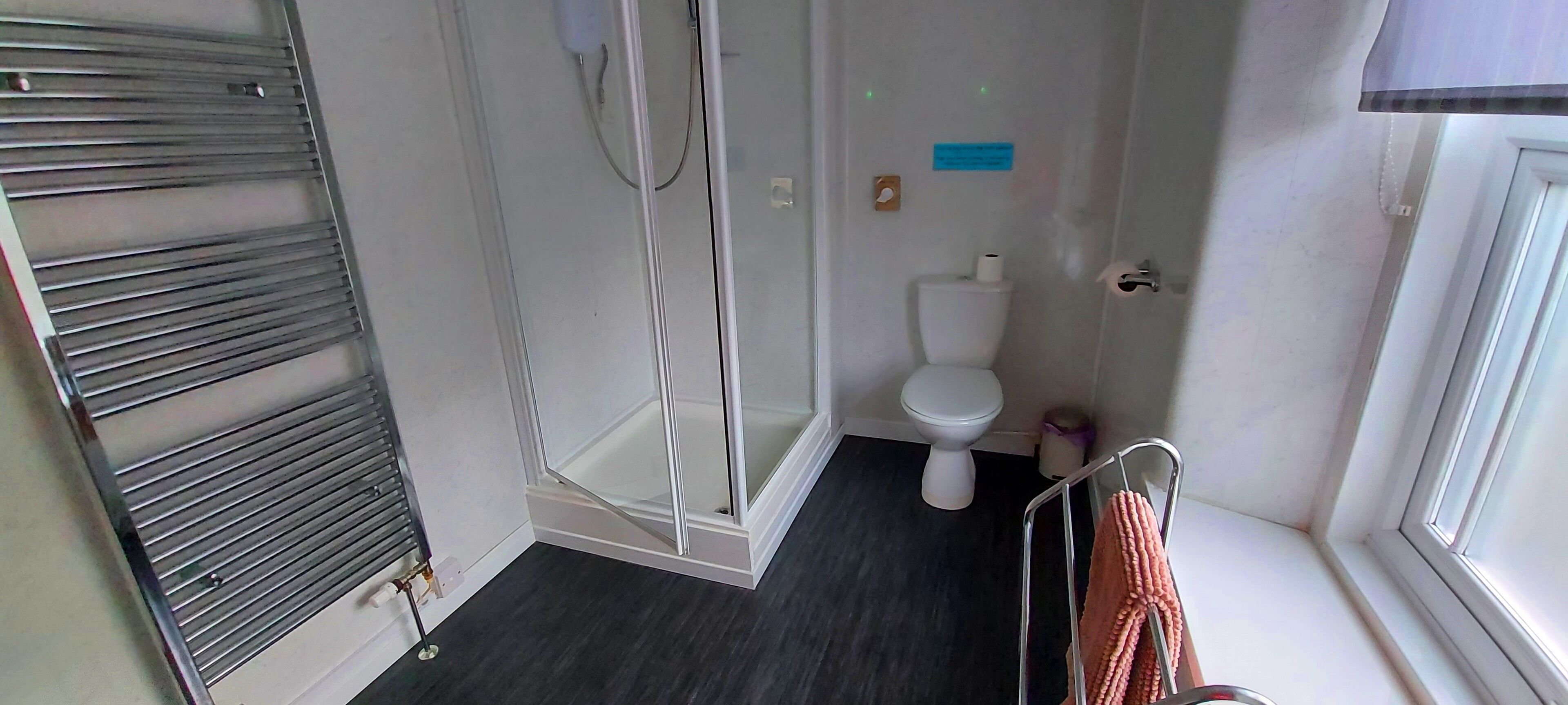 A compact bathroom with a shower, toilet, and a towel rack by the window.